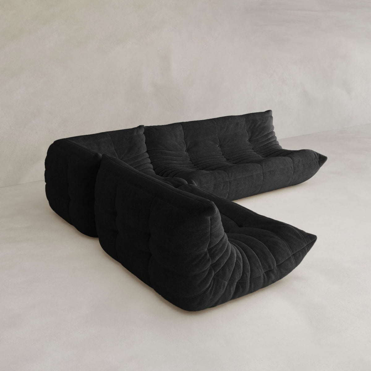 The Rolo Lounge Three Piece Sofa, a modern modular black sectional with deep plush cushions, sits on a light minimalist floor against a neutral wall, highlighting its mid-century design influences.