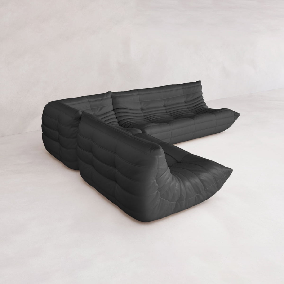 The Rolo Lounge Three Piece Sofa, a modular black leather sectional with plush tufted cushions, is arranged in an L-shape on a white minimalist floor against a light-colored wall.