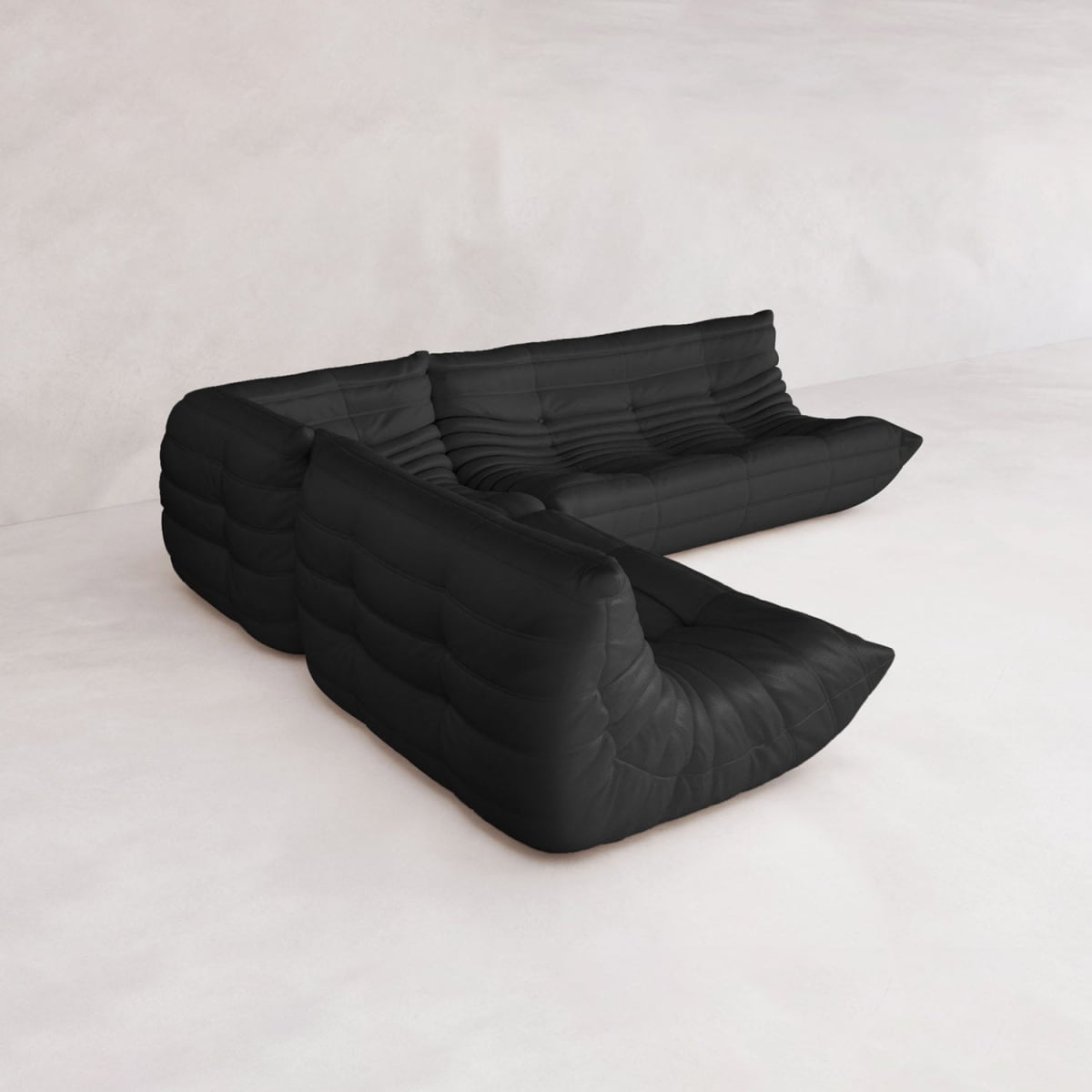 The Rolo Lounge Three Piece Sofa, a modern black modular design with tufted upholstery and no arms, inspired by mid-century style, is placed on a light floor against a minimalist white wall.