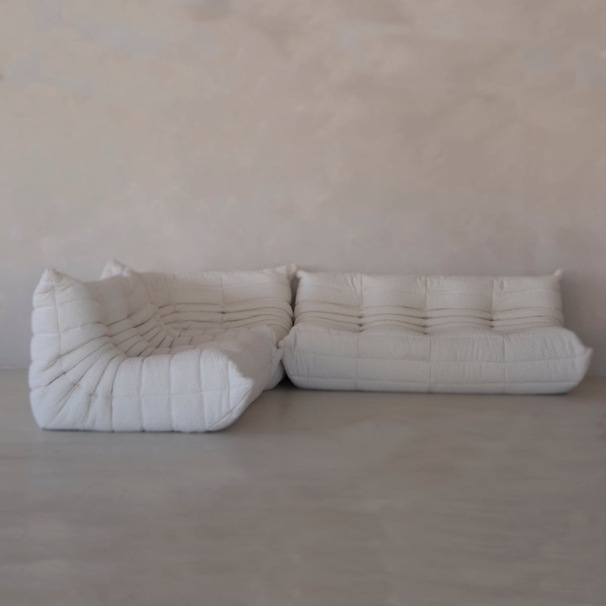 The Rolo Lounge Three Piece Sofa, with its modern white tufted design and quilted cushions, showcases mid-century style in a bright room with light walls and a sleek gray floor.