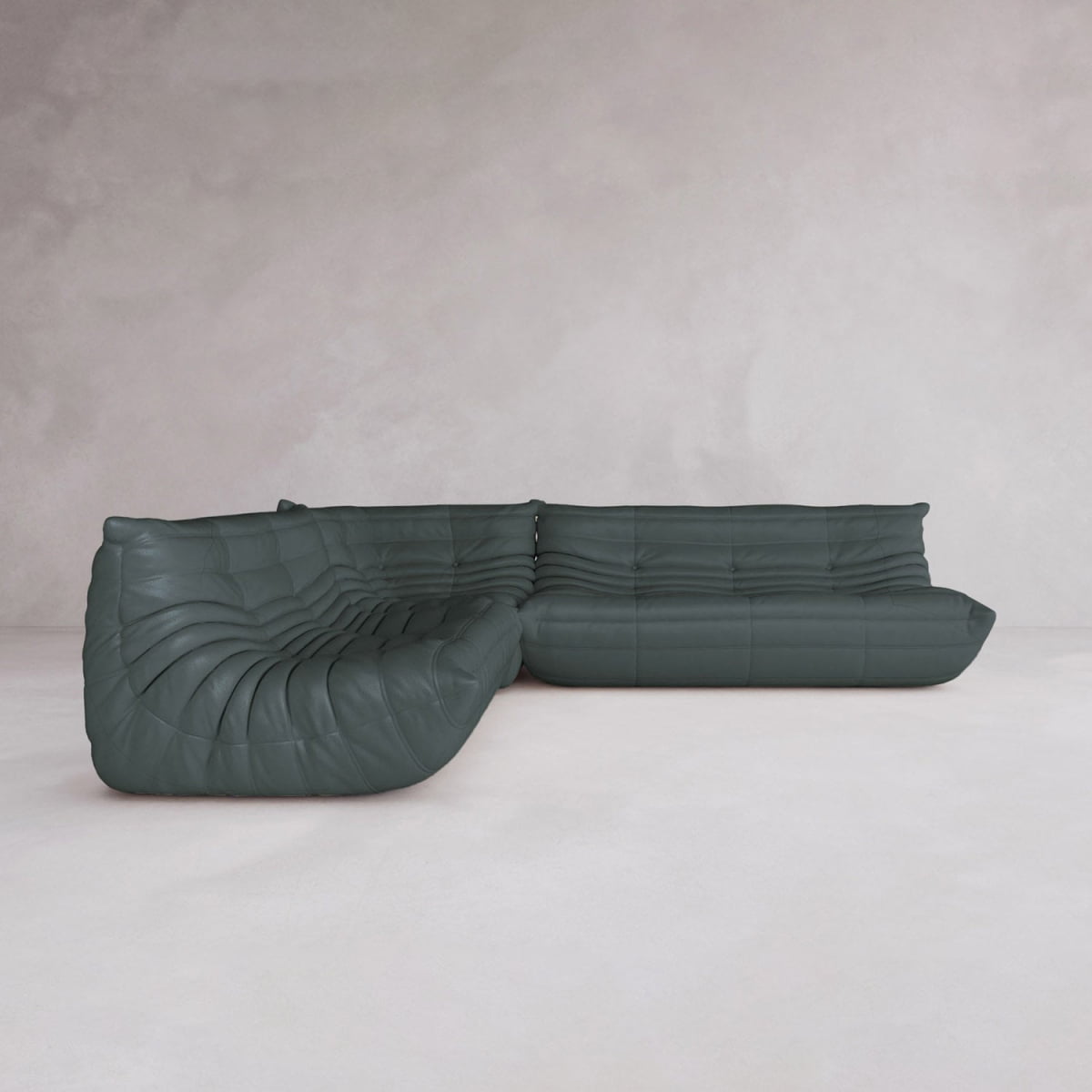 The Rolo Lounge Three Piece Sofa, a modern dark green L-shaped sectional with tufted cushions and mid-century flair, sits on a light-colored floor against a pale wall.