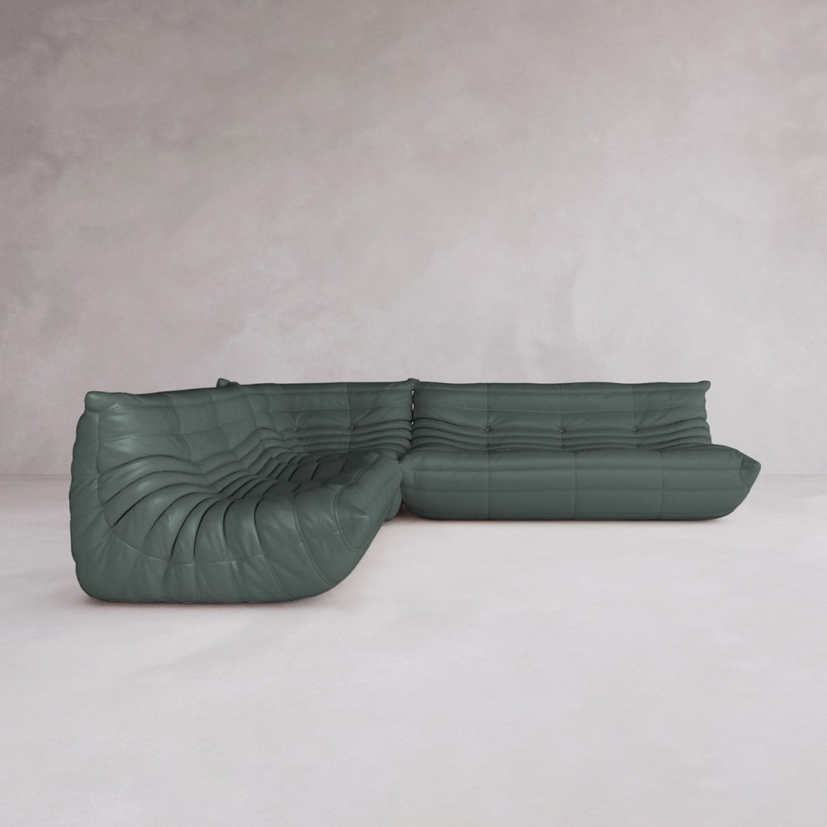 The Rolo Lounge Three Piece Sofa features a modern dark green, low, tufted design with soft, rounded edges as part of a modular system, placed on a light gray floor against a textured pale gray wall.