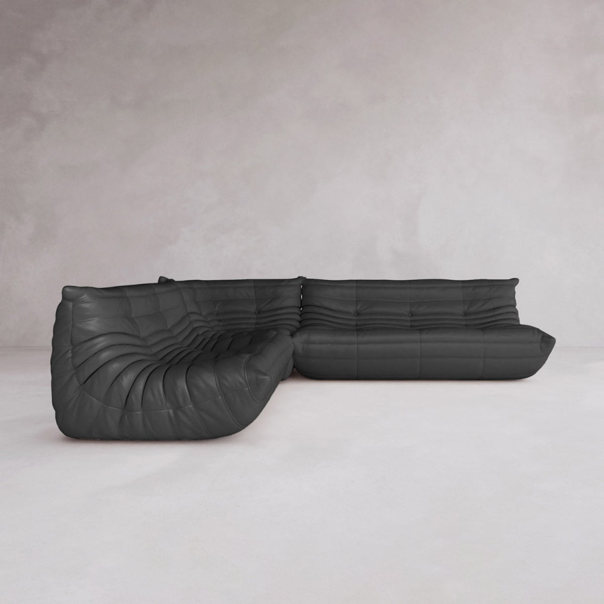 The Rolo Lounge Three Piece Sofa, a modern black L-shaped sectional with deep plush cushions and mid-century design, sits on a plain light floor against a minimalist light grey wall.