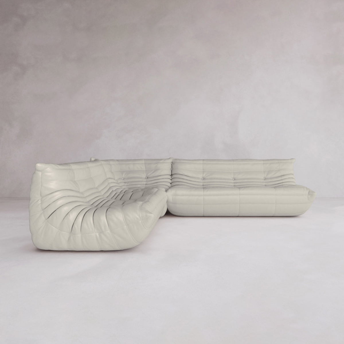 The Rolo Lounge Three Piece Sofa—a modern, light gray sectional with a tufted, curvy design and mid-century flair—sits in an empty room with light walls and flooring.