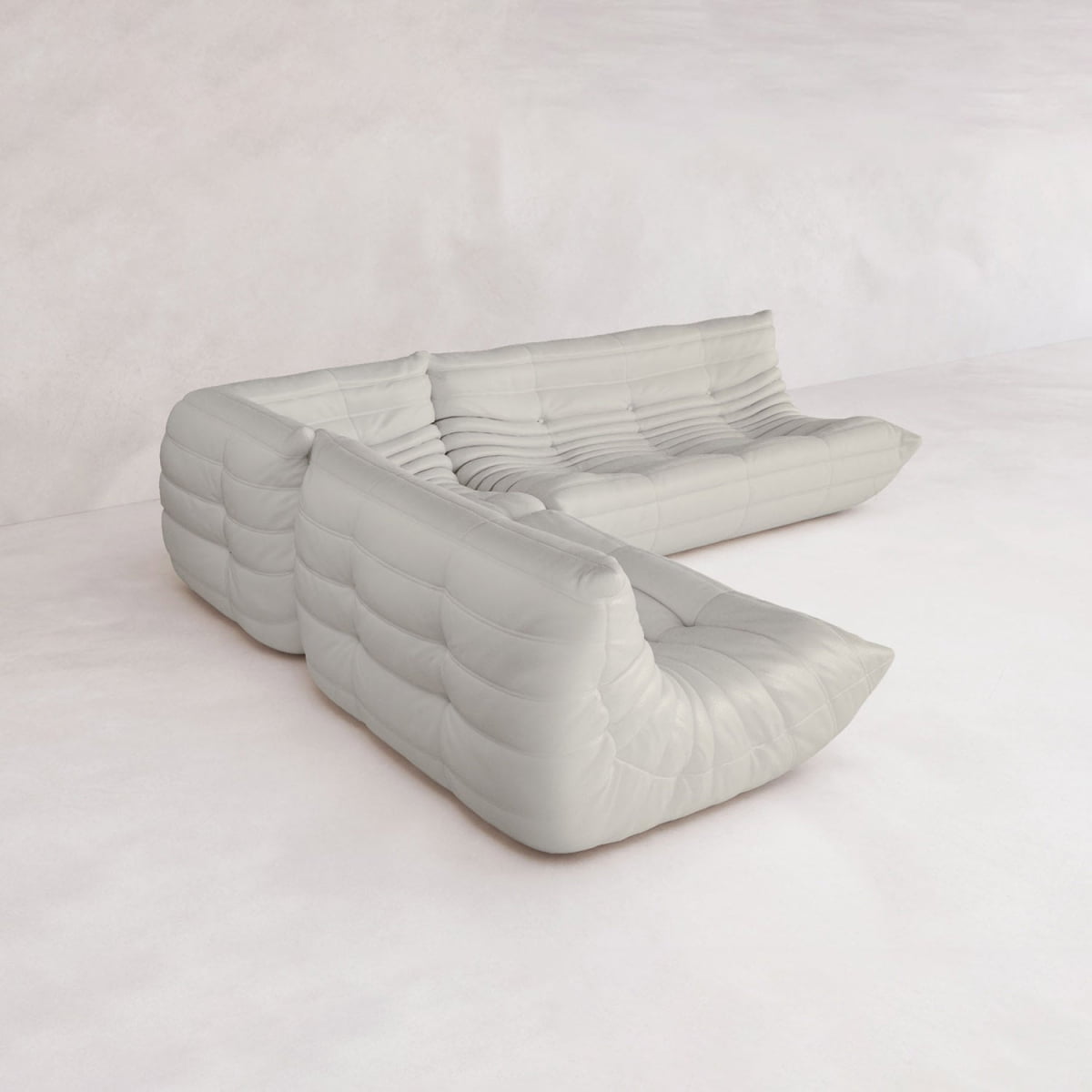The Rolo Lounge Three Piece Sofa, a modern low-profile white sectional with plush tufted cushions and mid-century flair, sits on a light floor in a minimal, softly lit room with pale walls.
