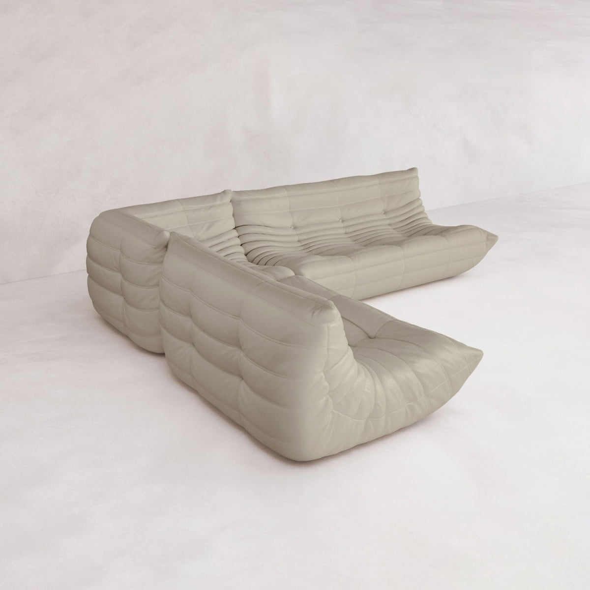 The Rolo Lounge Three Piece Sofa, a modern light beige sectional with low tufted seats and mid-century details, is featured in a minimalist room with smooth floors and plain walls.