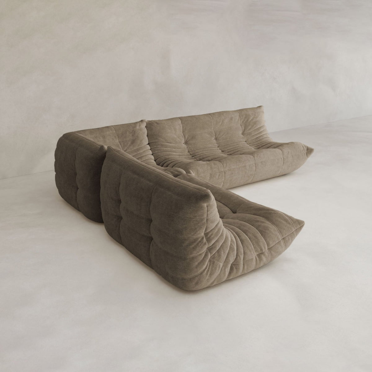The Rolo Lounge Three Piece Sofa, a modern brown sectional with tufted cushions, sits against a plain light wall and floor in a minimalistic room.