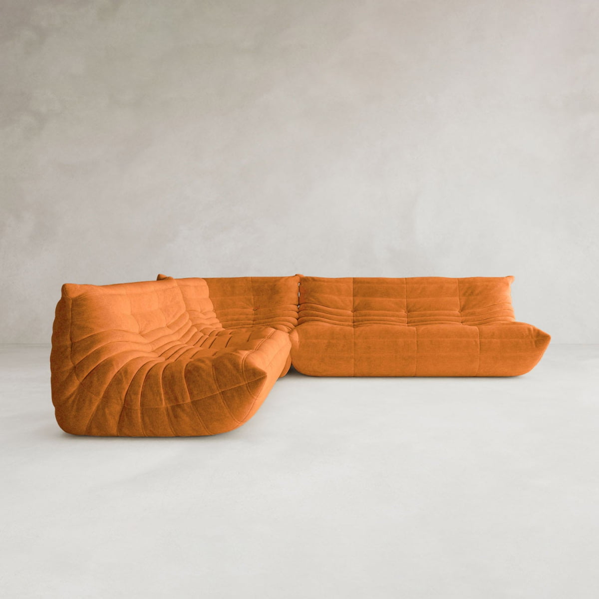 The Rolo Lounge Three Piece Sofa, a modern modular orange piece with tufted, wavy design and deep cushioned seats, sits on a smooth light floor against a plain light gray wall.