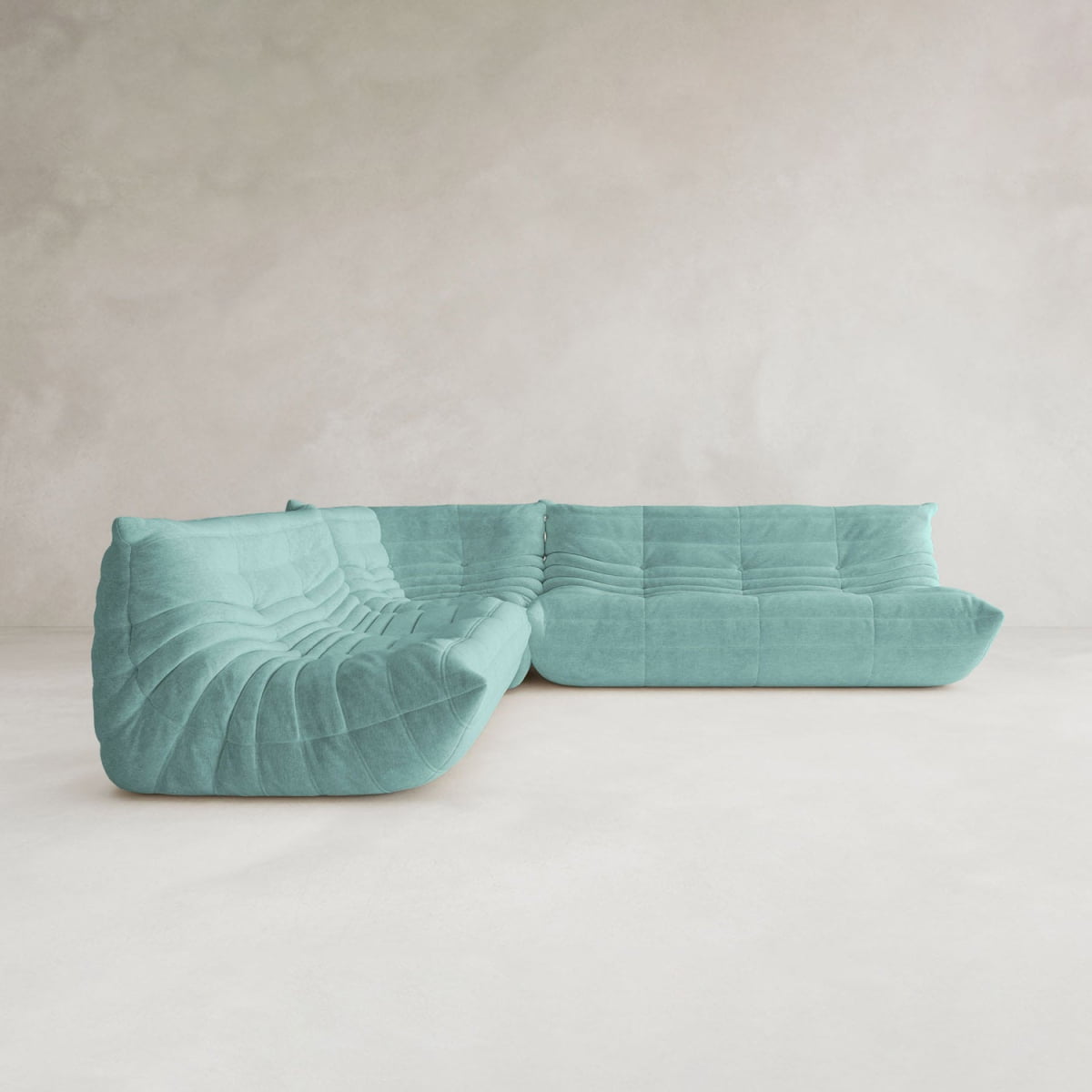 The Rolo Lounge Three Piece Sofa, featuring a modern modular design and quilted plush texture in turquoise, sits on a light minimalist floor against a pale textured wall.