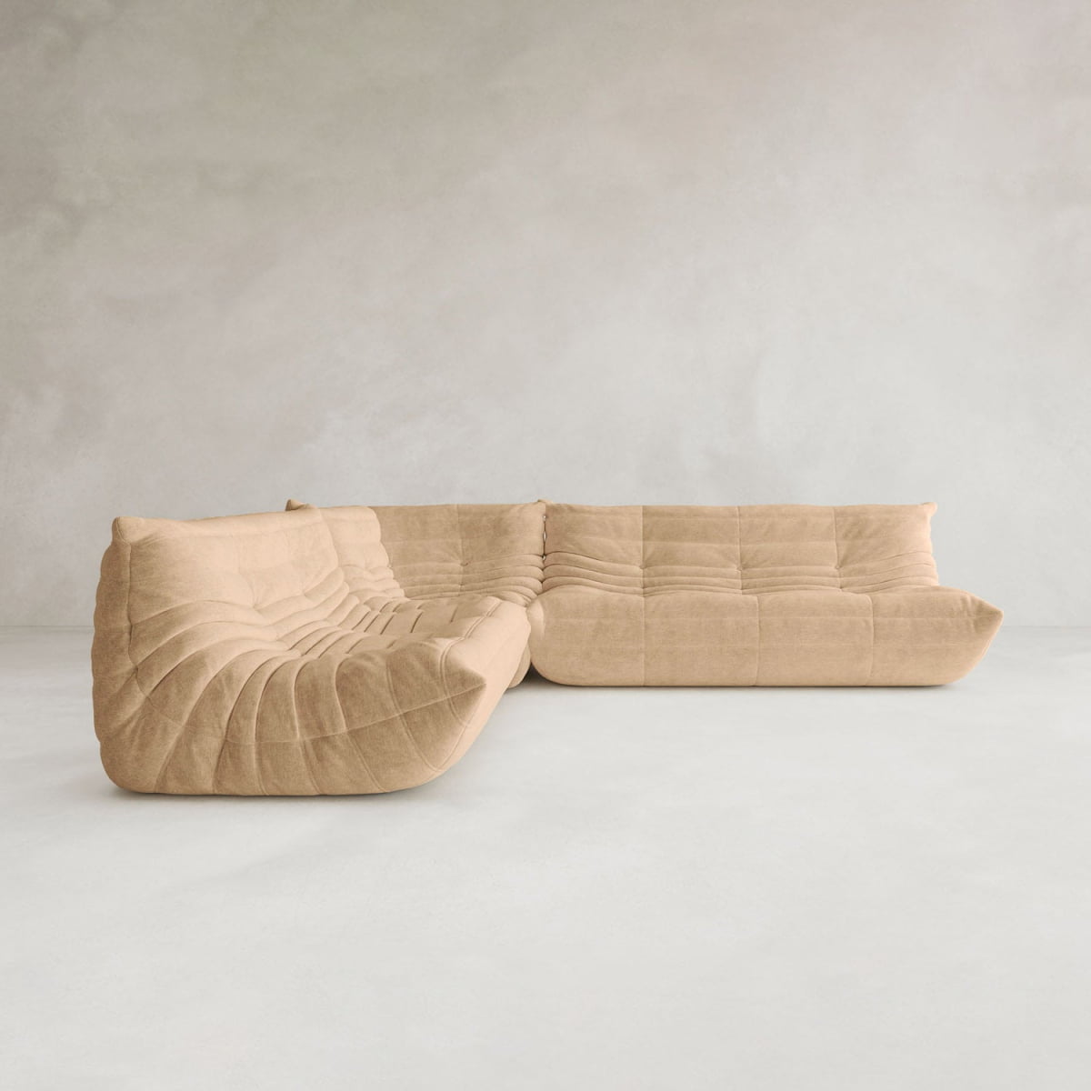 The Rolo Lounge Three Piece Sofa, featuring deep, plush tufted upholstery and a modern mid-century design in beige, is placed in a minimal, spacious room with light gray textured walls and flooring.