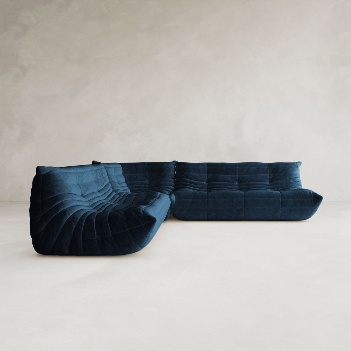 The Rolo Lounge Three Piece Sofa, in deep blue with curved, tufted upholstery, brings mid-century style to a minimalistic room with its plush design set against a pale wall and light floor.