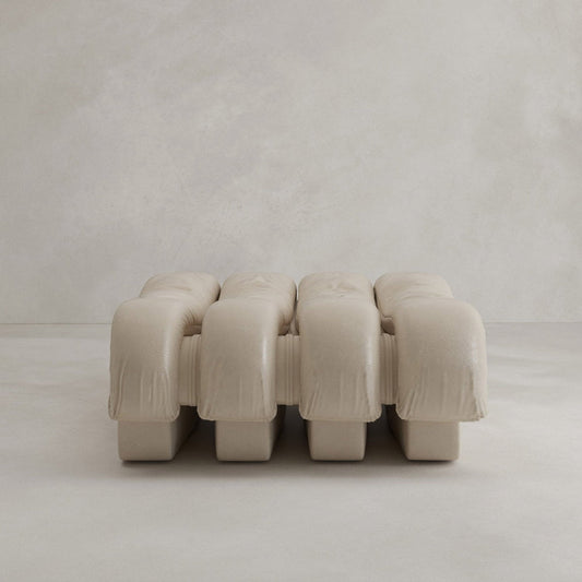 The Serpenti Sofa Ottoman is a modern, minimalist beige bench with three plush cushions and a textured finish, designed to seamlessly complement any modular setup, shown here against a plain light background.
