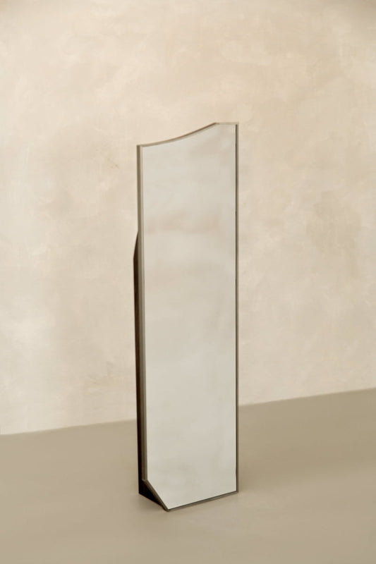 The Shard Mirror S, a tall and narrow mirror with a slightly irregular, angled top edge, brings modern elegance as it stands freestanding against a neutral beige background.