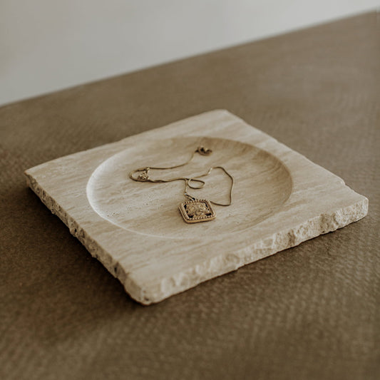 The Solara Charger rests on a square, textured stone tray atop a brown surface, highlighting its natural elegance.