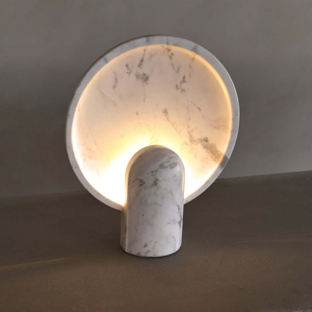 The Stella Lamp in Blanco Marble features a circular, upright disc crafted from white marble and softly backlit to create a calming ambiance with a warm glow against neutral backgrounds.