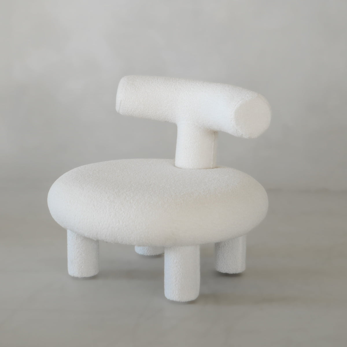 The Teddy Chair Rental is a modern, minimalist Neotenic chair with a round seat, cylindrical backrest, and four thick legs in soft white fabric—a luxury piece that makes a bold statement against a light grey background.