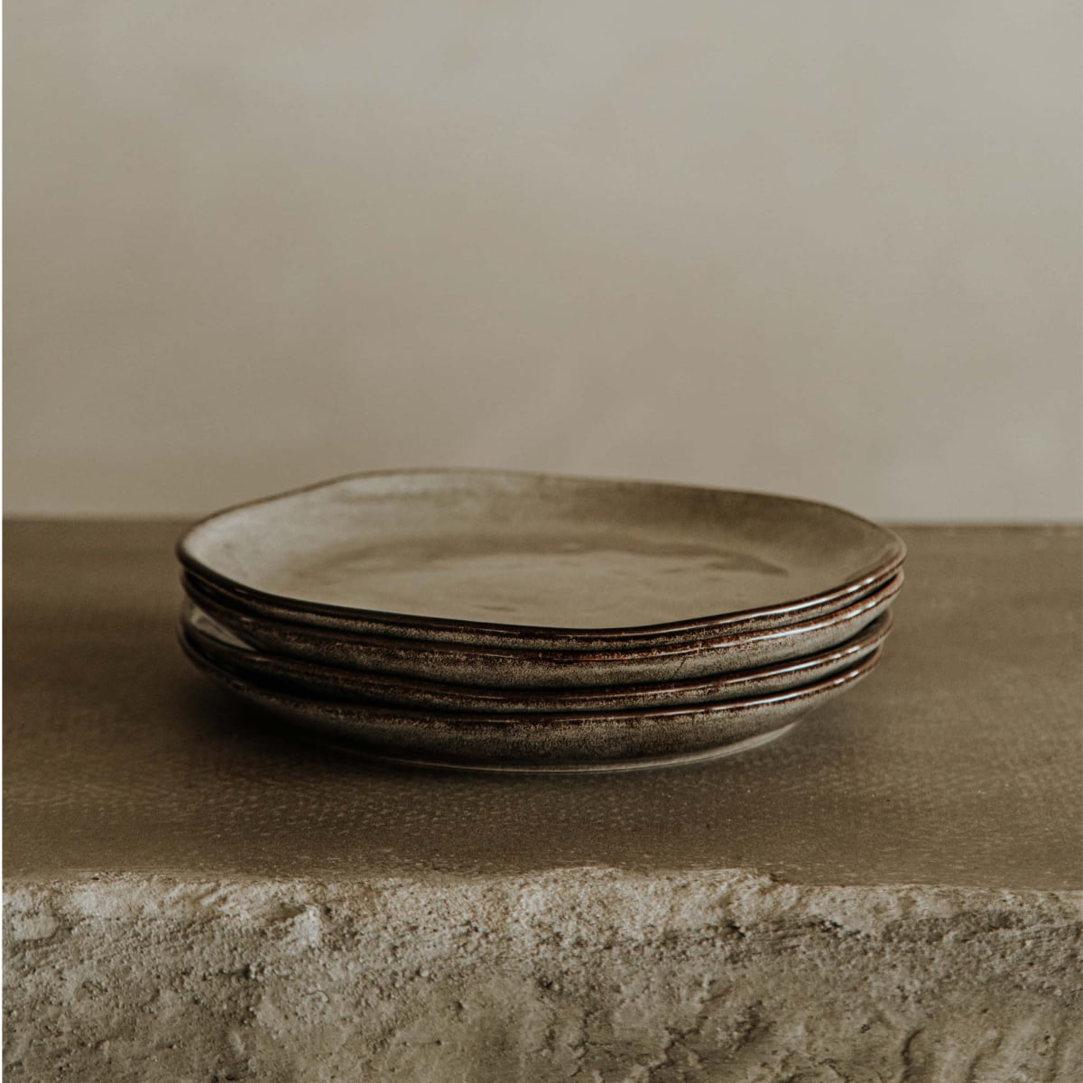 A stack of four Tundra Glazed Dish Large ceramic plates sits on a textured stone surface, set against a neutral beige background.
