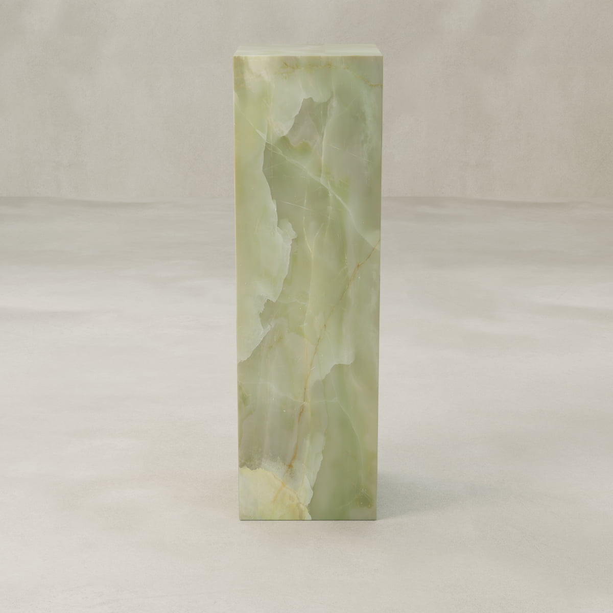 The Verdaine Onyx Tall Tower Plinth showcases translucent green onyx with natural veining in a rectangular design, set on a light textured surface and neutral background for a serene, standalone statement.