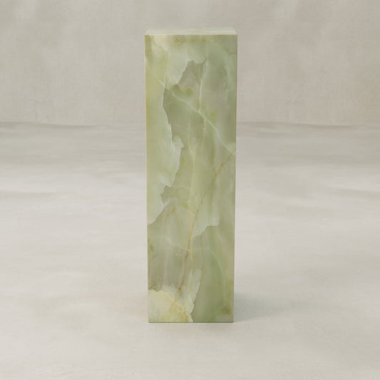The Verdaine Onyx Tall Tower Plinth showcases translucent green onyx with natural veining in a rectangular design, set on a light textured surface and neutral background for a serene, standalone statement.