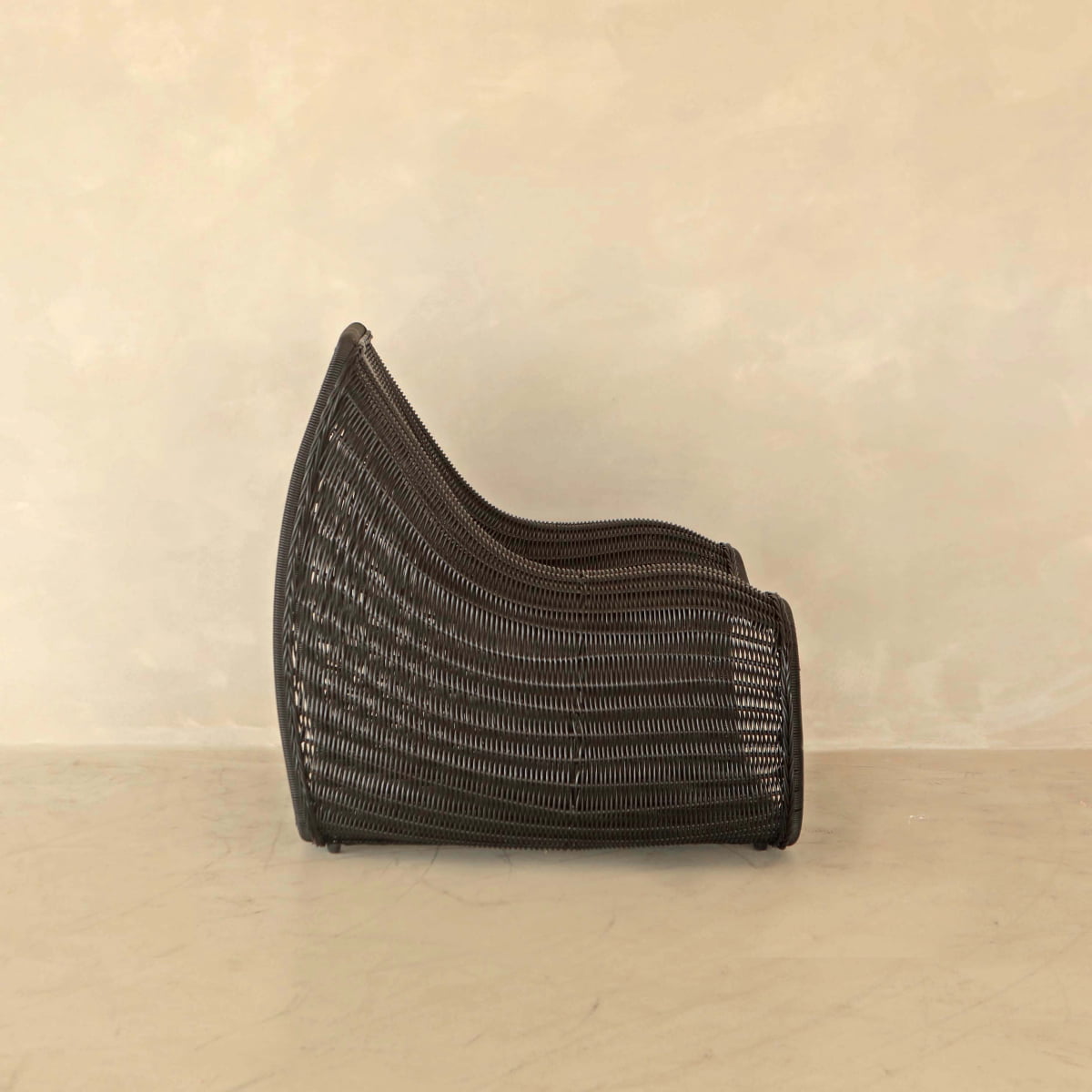 A side view of the Wicker Chair, featuring modern dark brown PU rattan with a curved back and base—ideal for outdoor relaxation—set against a plain beige background.