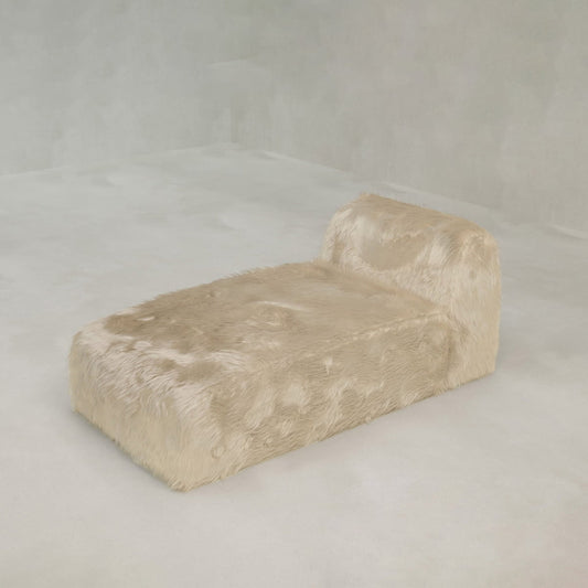 The Yeti Chaise Lounge, upholstered in soft beige faux fur, adds luxurious comfort and style to a minimalist room with light walls and flooring.