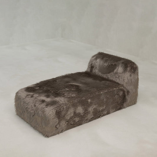 The Yeti Chaise Lounge, upholstered in plush brown faux fur, provides luxurious comfort and sits on a light-colored floor against a simple, pale backdrop.