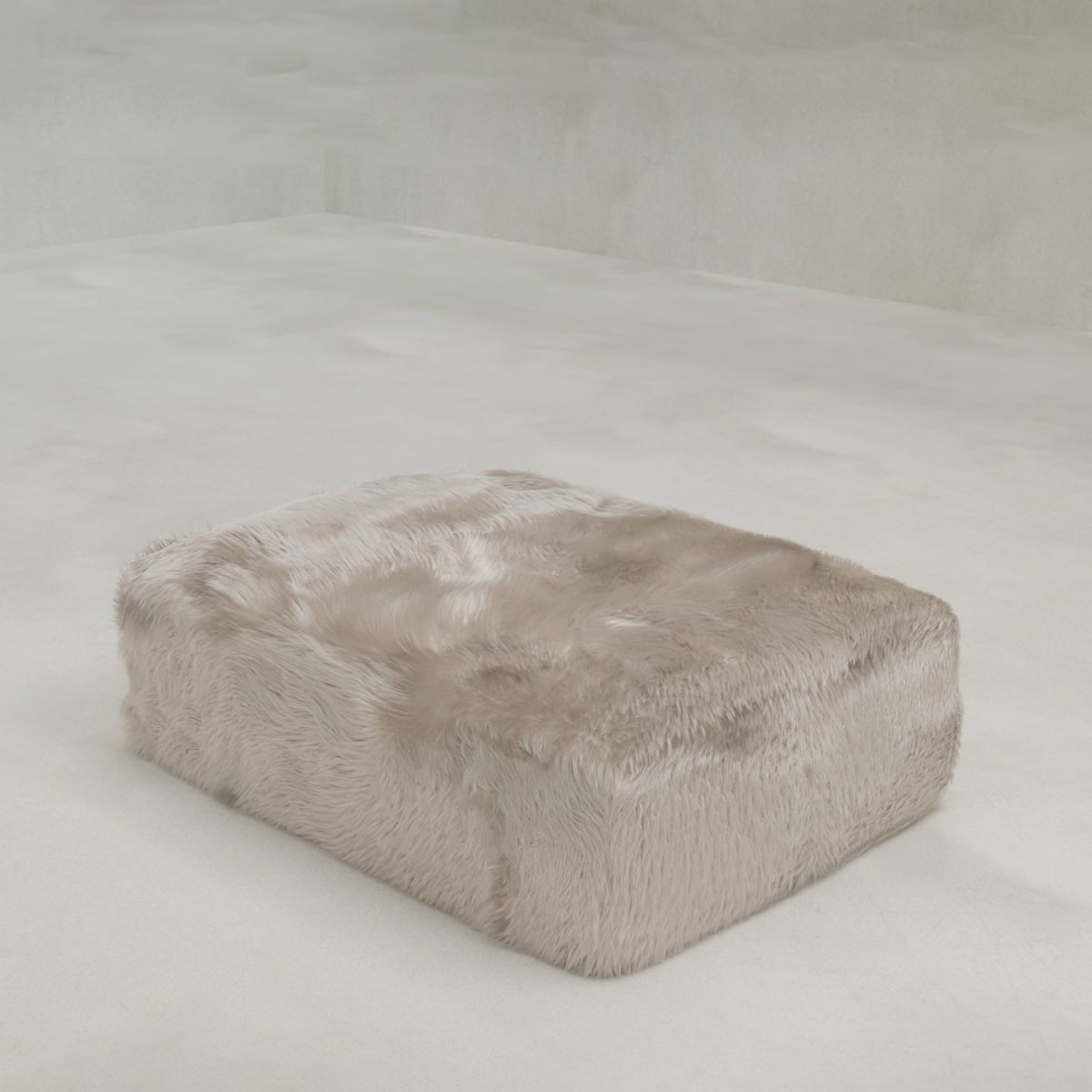 The large, rectangular Yeti Ottoman features plush faux fur upholstery and stands on a smooth, pale floor in a minimalist room with light-colored walls.