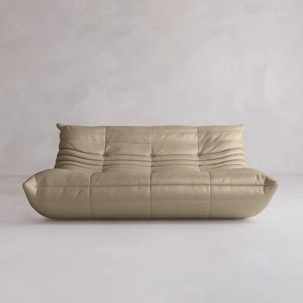 The Rolo Lounge Three Seater is a modern, beige, armless leather sofa with a low back and deep cushioned seat in subtle mid-century style, set against a plain light gray wall and floor.