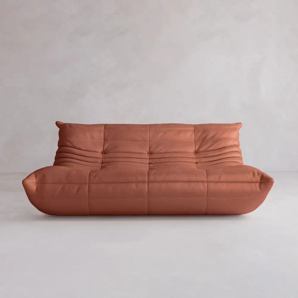 The Rolo Lounge Three Seater is a modern, armless brown leather sofa with mid-century design, low plush profile, and visible horizontal and vertical stitching, set against a plain light grey background.