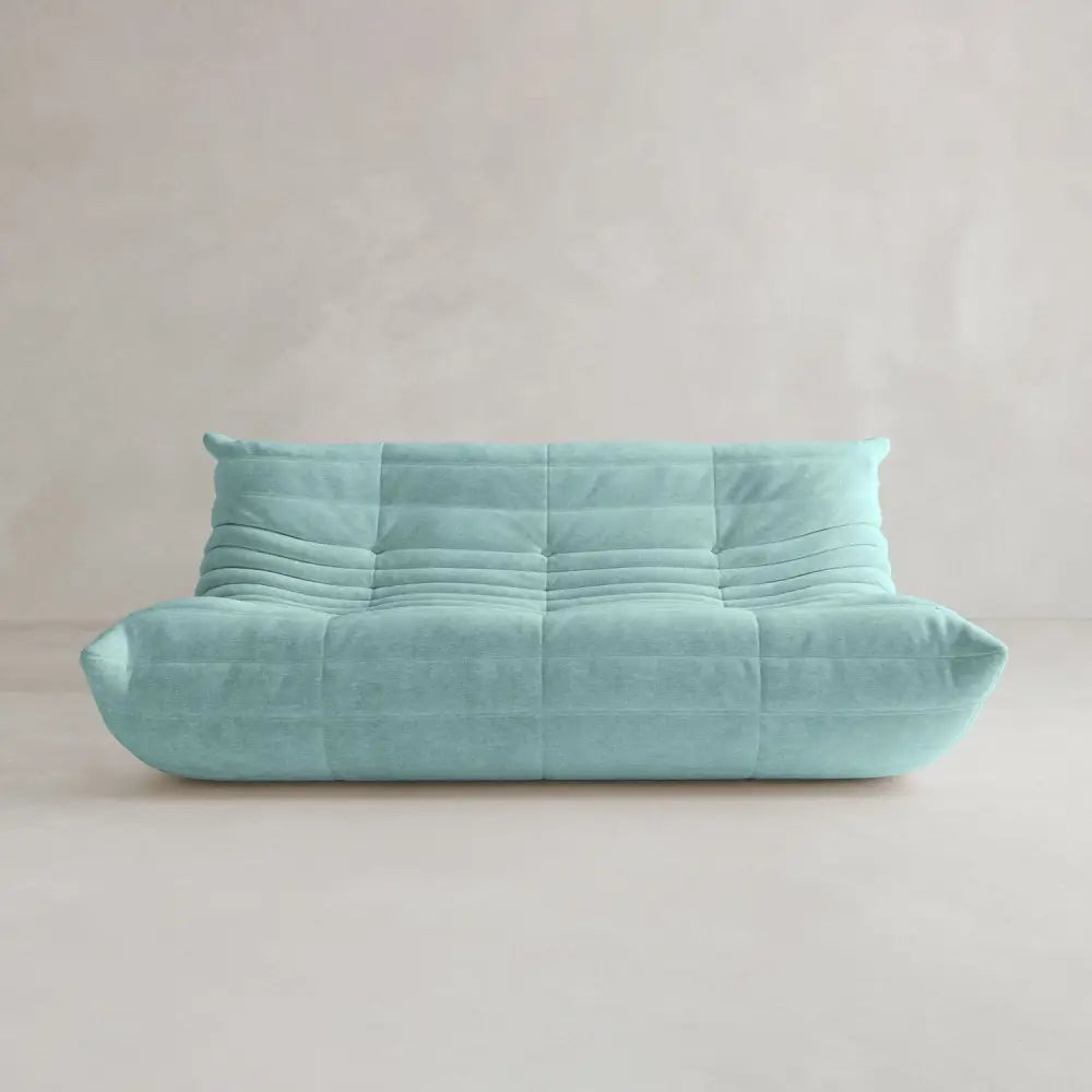 The Rolo Lounge Three Seater is a modern, turquoise, armless sofa with a plush quilted design and subtle mid-century influences, shown against a plain, light-colored wall and floor.