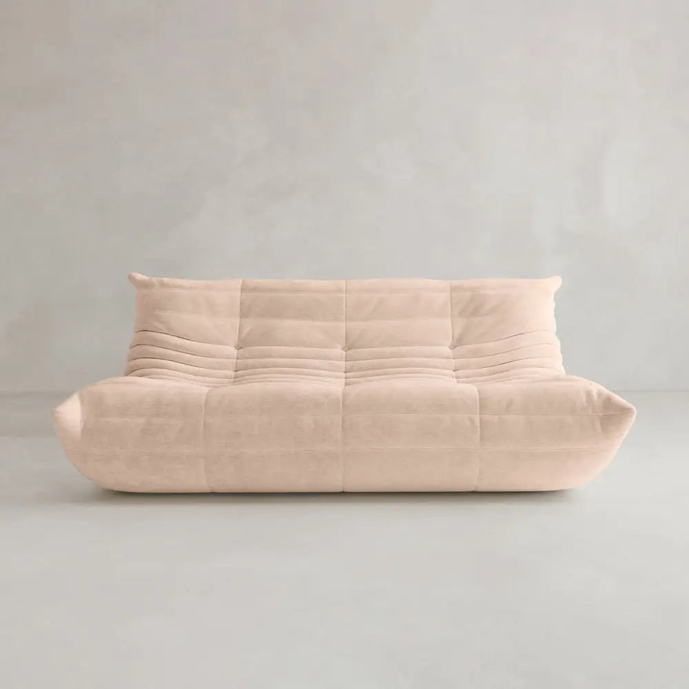 The Rolo Lounge Three Seater is a beige contemporary modular sofa with a low backrest, deep seat, and soft quilted upholstery, shown against a plain light gray wall and floor.