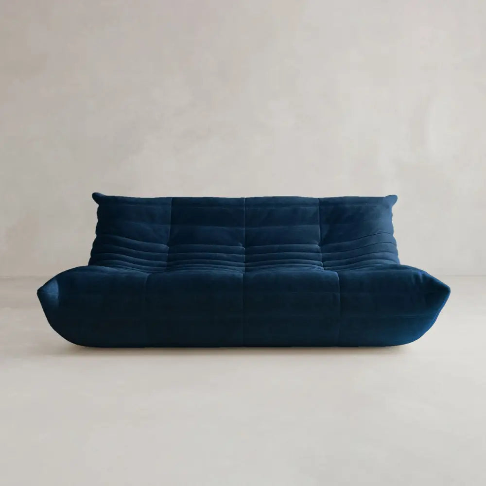 The Rolo Lounge Three Seater, a modern deep blue, armless sofa with a low back and tufted plush cushions, adds mid-century flair to a light floor and neutral backdrop.