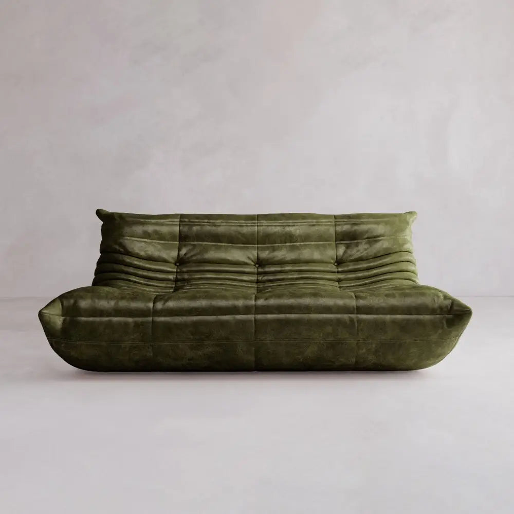 The Rolo Lounge Three Seater is a modern olive green sofa with mid-century design, soft rounded edges, and gathered upholstery, set against a plain light wall and floor.