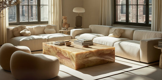 Modern luxury coffee table in honey onyx, styled with books and ceramics, placed in a neutral living room with curved sofas, sculptural lounge chairs, and arched windows.