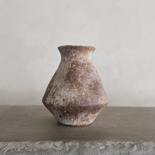 The Nami vase, featuring a rustic, weathered ceramic look and textured surface, sits on a rough gray stone ledge against a light gray backdrop—ideal for bringing farmhouse decor charm to your space.