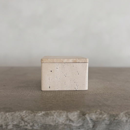 The Celeste Vault with Lid, a small rectangular beige stone box, rests on a textured gray surface against a plain, light background.