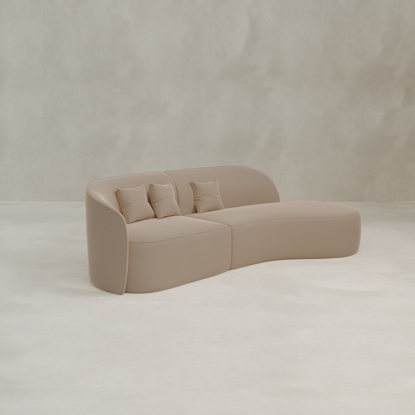 The Marlow Curved Modular Three Seater Sofa in beige velvet features three matching throw pillows and sits elegantly on a light, minimalist floor against a neutral textured wall.