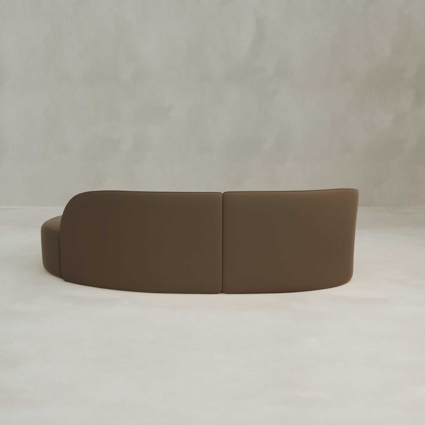 The Marlow Curved Modular Three Seater Sofa, featuring a modern design and low backrest, sits against a plain light grey textured wall, capturing a minimalistic aesthetic.