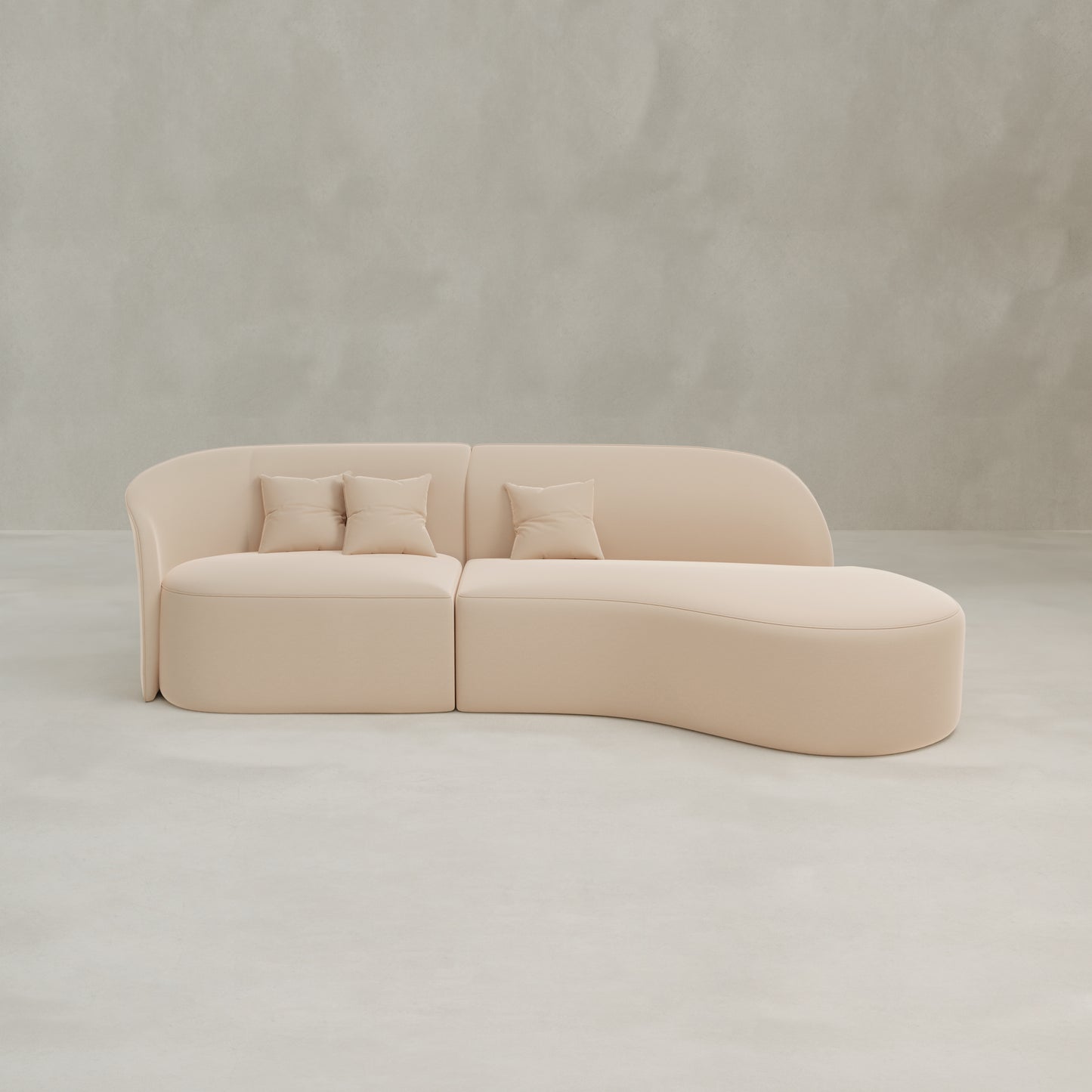 The Marlow Curved Modular Three Seater Sofa, featuring luxurious beige upholstery and three matching throw pillows, sits on a light gray floor against a plain, light-colored wall.