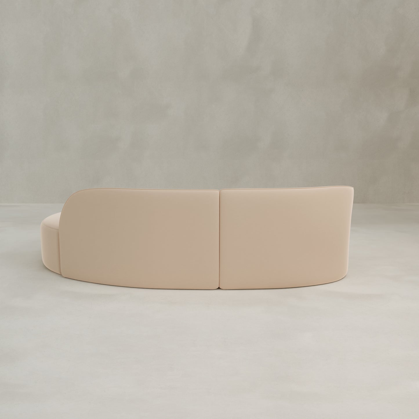 The Marlow Curved Modular Three Seater Sofa, featuring luxurious velvet upholstery, is placed against a light gray textured wall on a pale floor and viewed from the back.