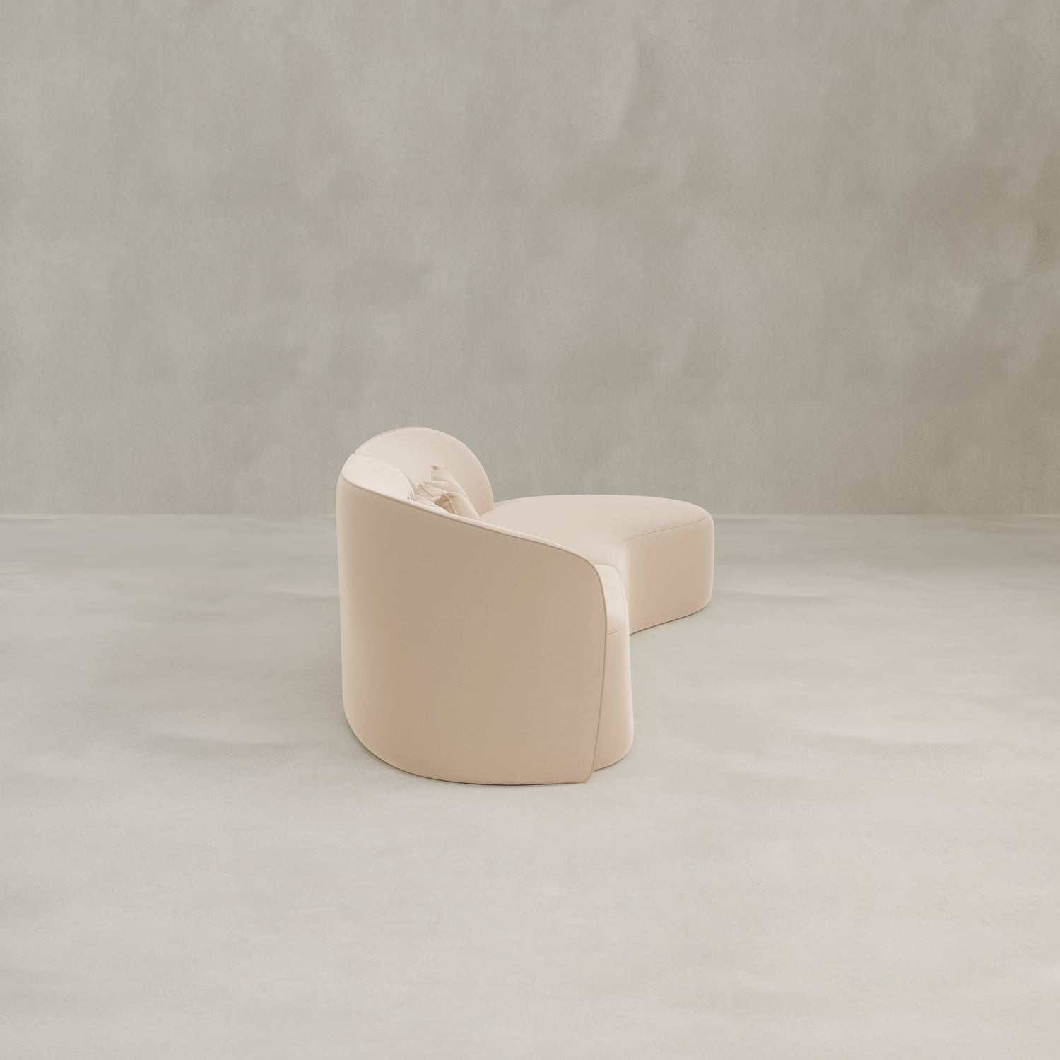 The Marlow Curved Modular Three Seater Sofa, featuring luxurious beige upholstery and soft, rounded edges, sits on a smooth light grey floor against a plain, textured grey wall.