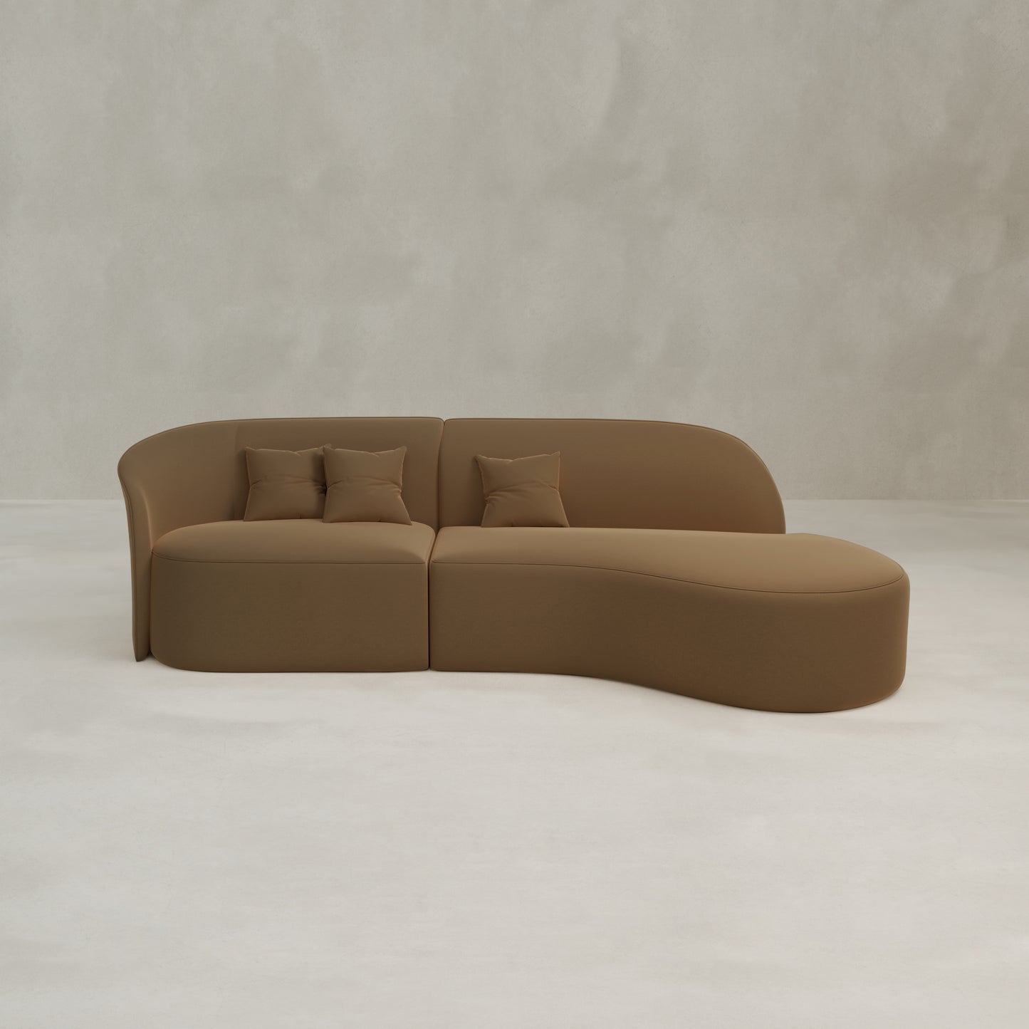 The Marlow Curved Modular Three Seater Sofa features a modern, minimalist velvet design with an asymmetrical shape and three matching pillows, shown against a light gray textured wall and a pale floor.