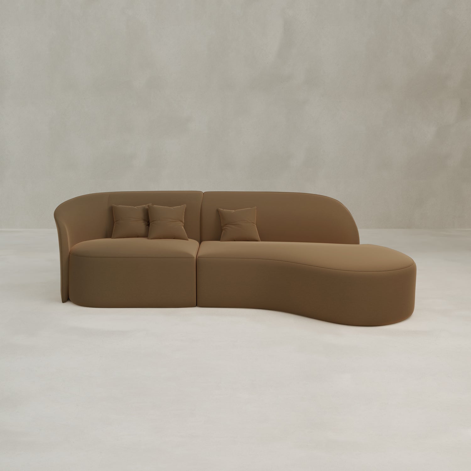 The Marlow Curved Modular Three Seater Sofa features a modern, minimalist velvet design with an asymmetrical shape and three matching pillows, shown against a light gray textured wall and a pale floor.