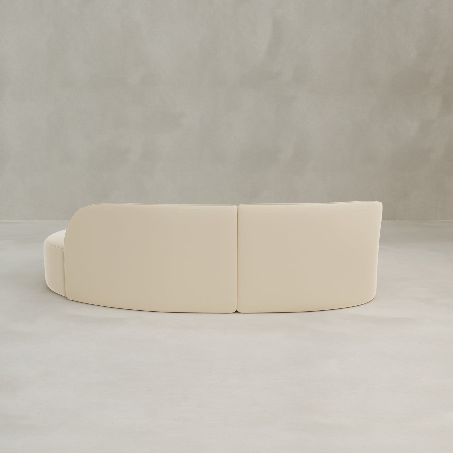 The Marlow Curved Modular Three Seater Sofa features modern cream velvet upholstery, shown from the back against a plain light gray textured wall and floor background.
