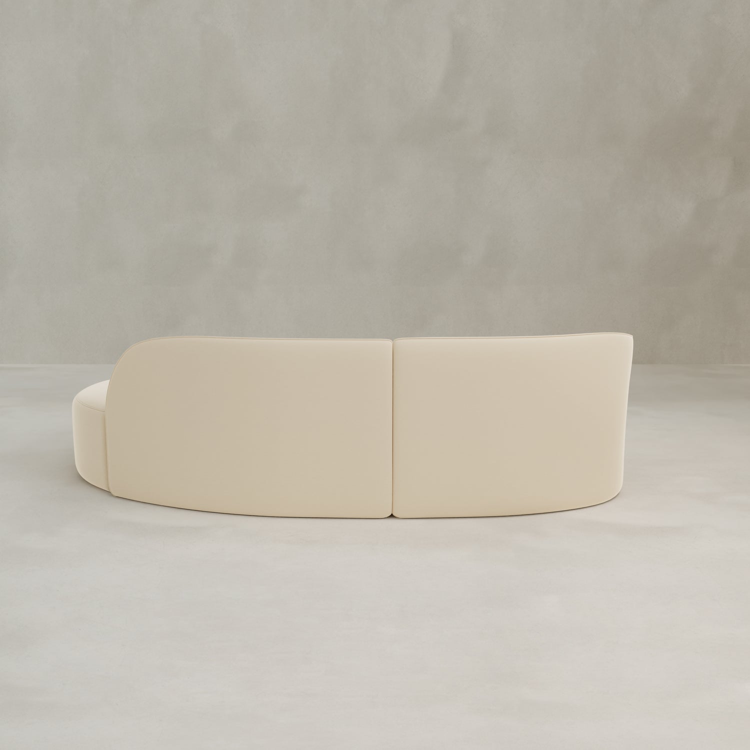 The Marlow Curved Modular Three Seater Sofa features modern cream velvet upholstery, shown from the back against a plain light gray textured wall and floor background.