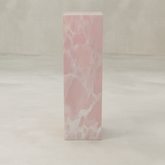 The Cora Tall Tower Plinth, a rectangular pink onyx piece with white veining, stands on a smooth light beige surface against a neutral background.