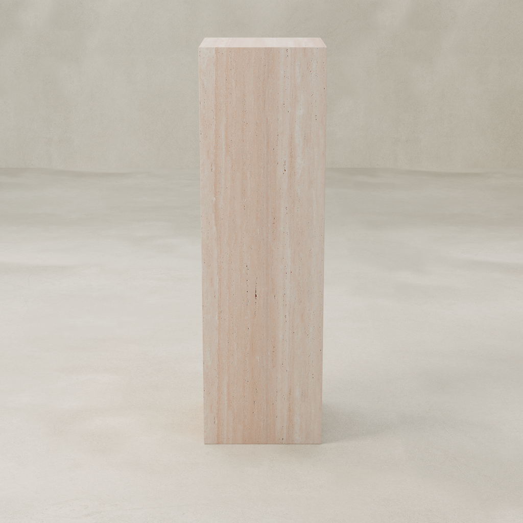 The Alessia Tall Tower Plinth, a rectangular piece crafted from light-colored travertine, stands on a neutral floor with a matching background and features subtle natural vertical lines and textures for a modern look.