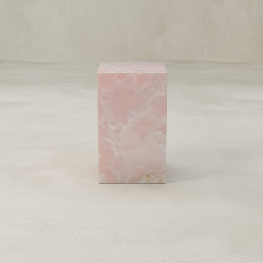 The Cora Tall Plinth, made from pink onyx with cloudy white and light brown veining, stands rectangular on a smooth, light floor against a beige background.