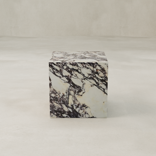 The Calacatta Cube Plinth, made from white Calacatta Viola marble with dramatic dark veining, rests on a smooth light surface against a plain backdrop—an elegant accent for refined interiors.