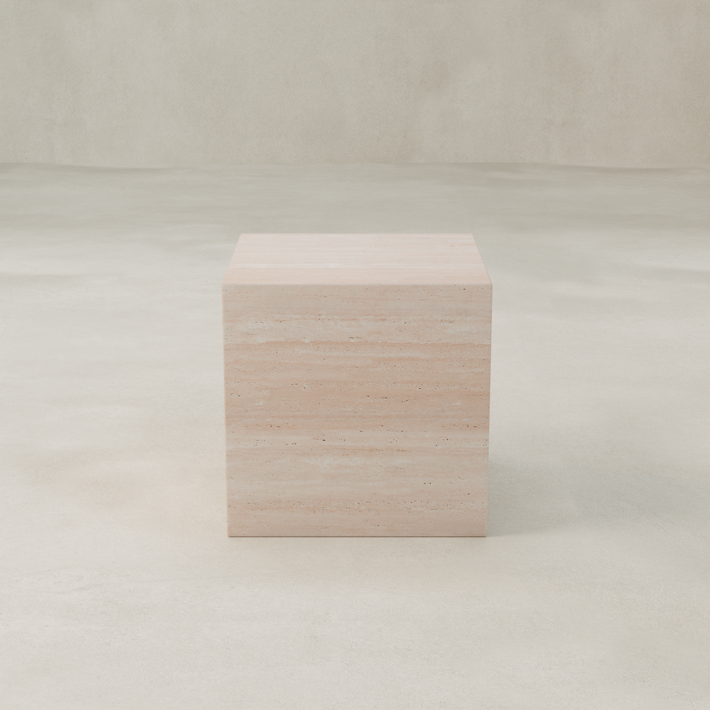 The Alessia Plinth, a modern large travertine stone cube, sits on a smooth cream surface against a matching neutral background.